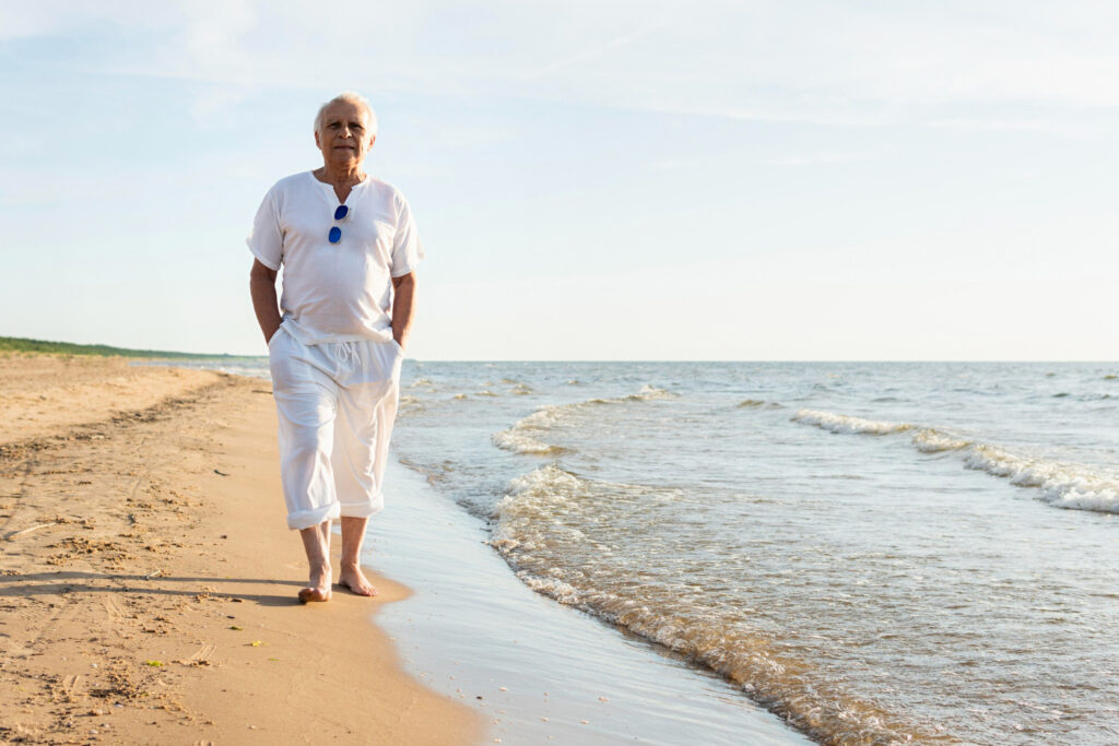 Ein älterer Herr geht am Strand gemütlich spazieren. Freuen Sie sich über aktuelle Angebote in unserem Haus.