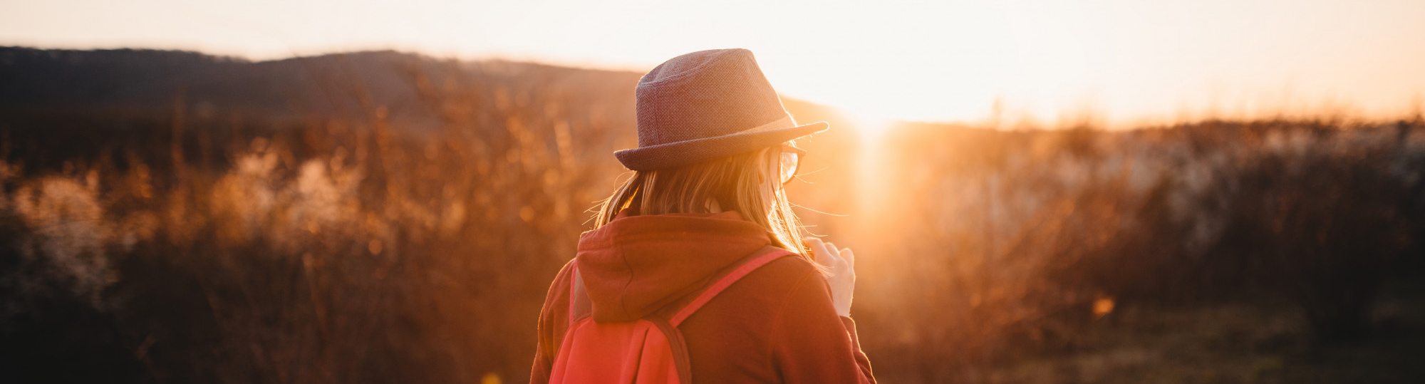 Eine junge wandert durch die Dünen in Richtung Sonnenuntergang.
